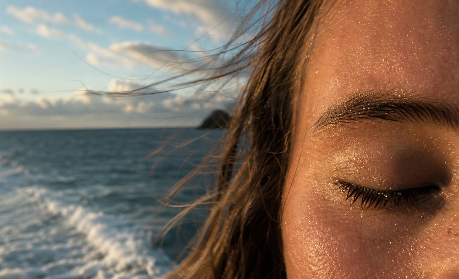 Visage les yeux fermés face à la mer au coucher du soleil, embruns et lumière dorée